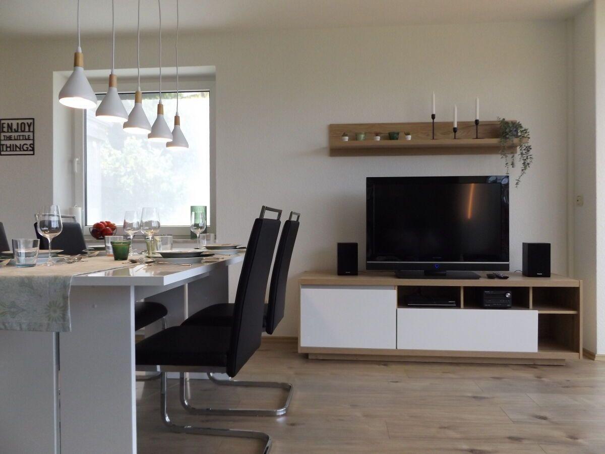 Dining area with table and chairs, TV on media unit and pendant lights.