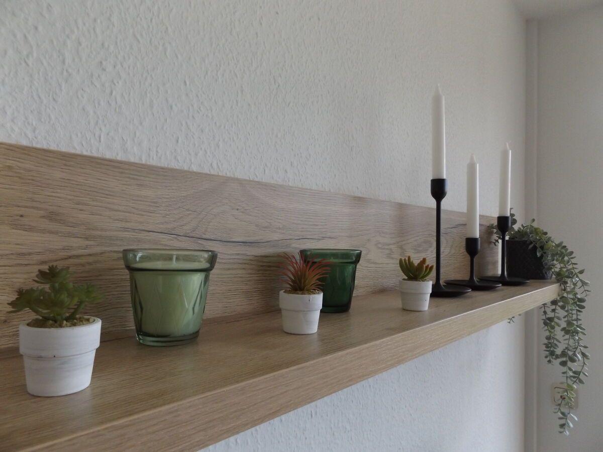 Wooden shelf with plants, candles, and glasses on the wall