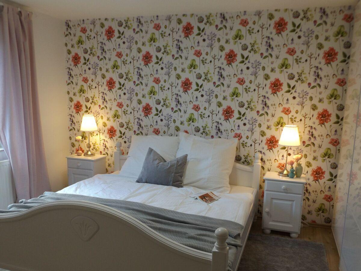 Bedroom with floral wallpaper, white bed, and nightstands with lamps.