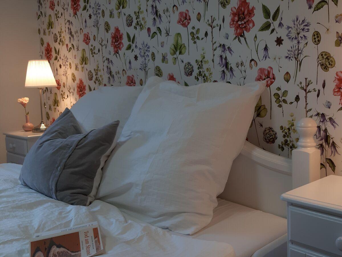 Double bed with pillows, nightstand, and floral wallpaper