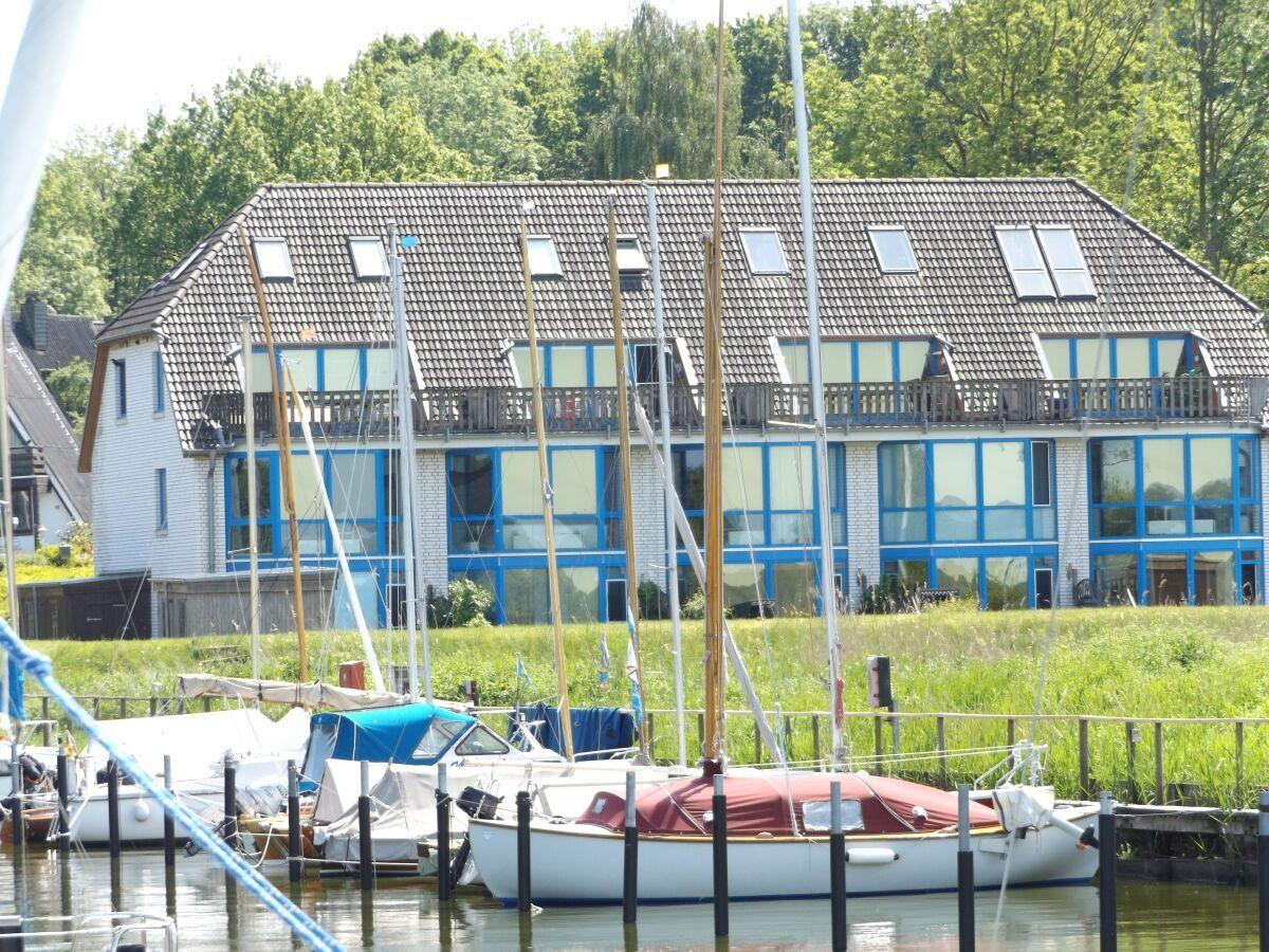 A house with blue windows and balcony, surrounded by boats and grass.