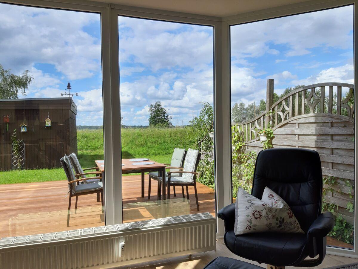 Large windows overlook a terrace with table and chairs. A black chair is in the foreground.