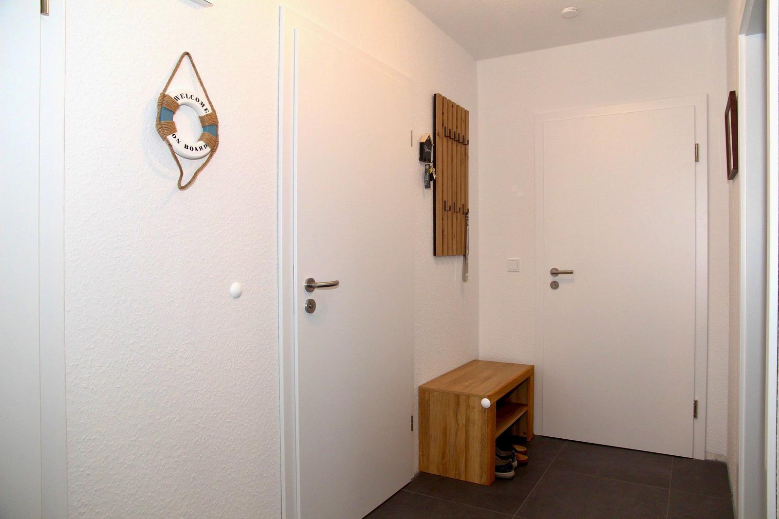 Eingangsbereich mit Holzbank, Wandgarderobe und Willkommensschild.