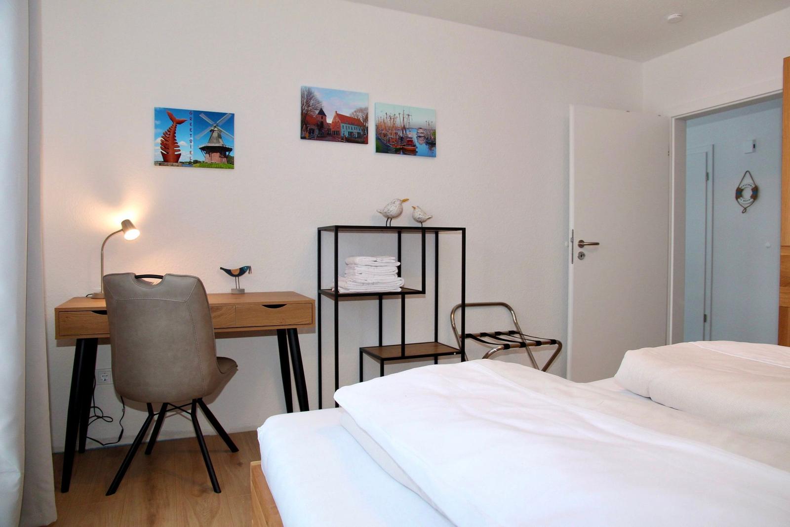 Schlafzimmer mit Bett, Schreibtisch und Wandbildern.