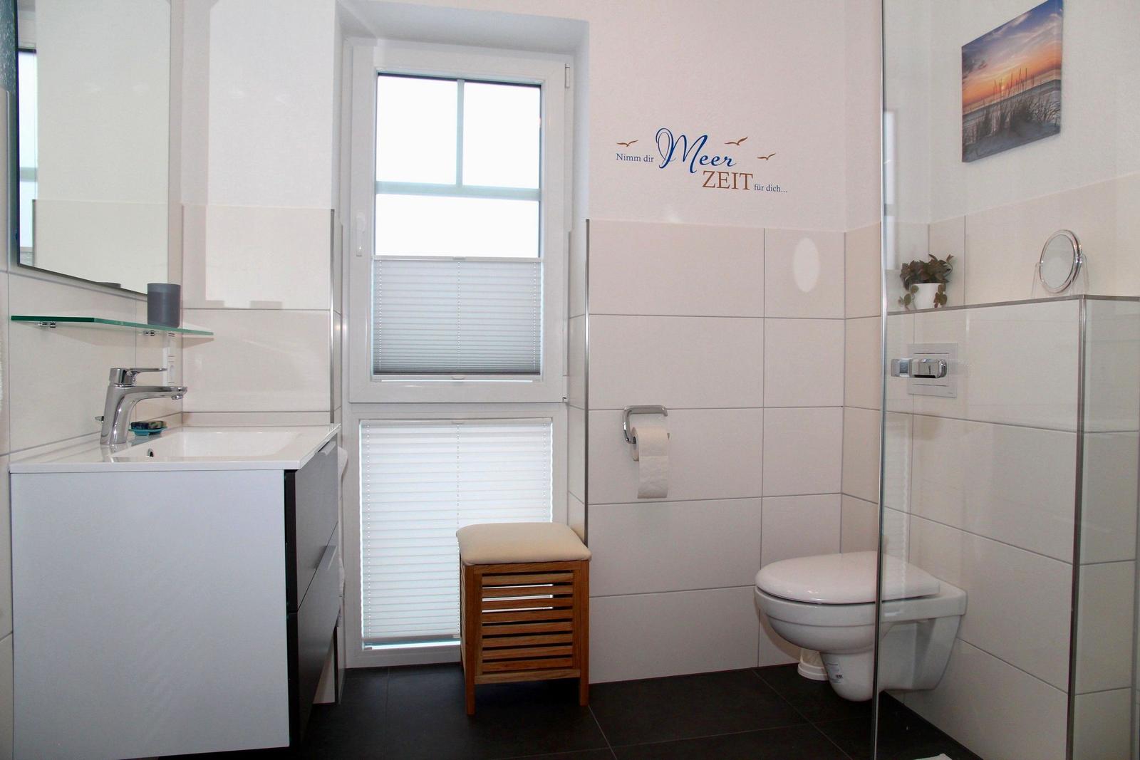 Badezimmer mit Waschbecken, Toilette und Dusche. Fenster mit Jalousie.