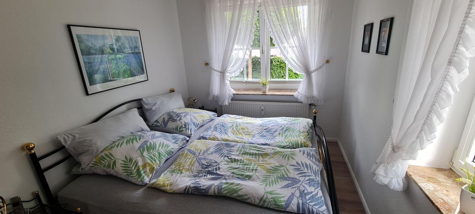 Schlafzimmer mit Doppelbett, Fenster und weißen Vorhängen.