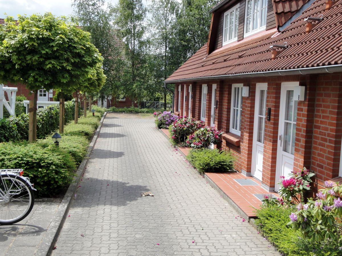 Gepflasterter Weg führt an roten Backsteinhäuser mit weißen Türen und Blumenbeeten vorbei.