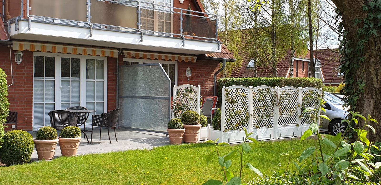 Haus mit Balkon, Terrasse und Garten mit weißen Lattenzaun.