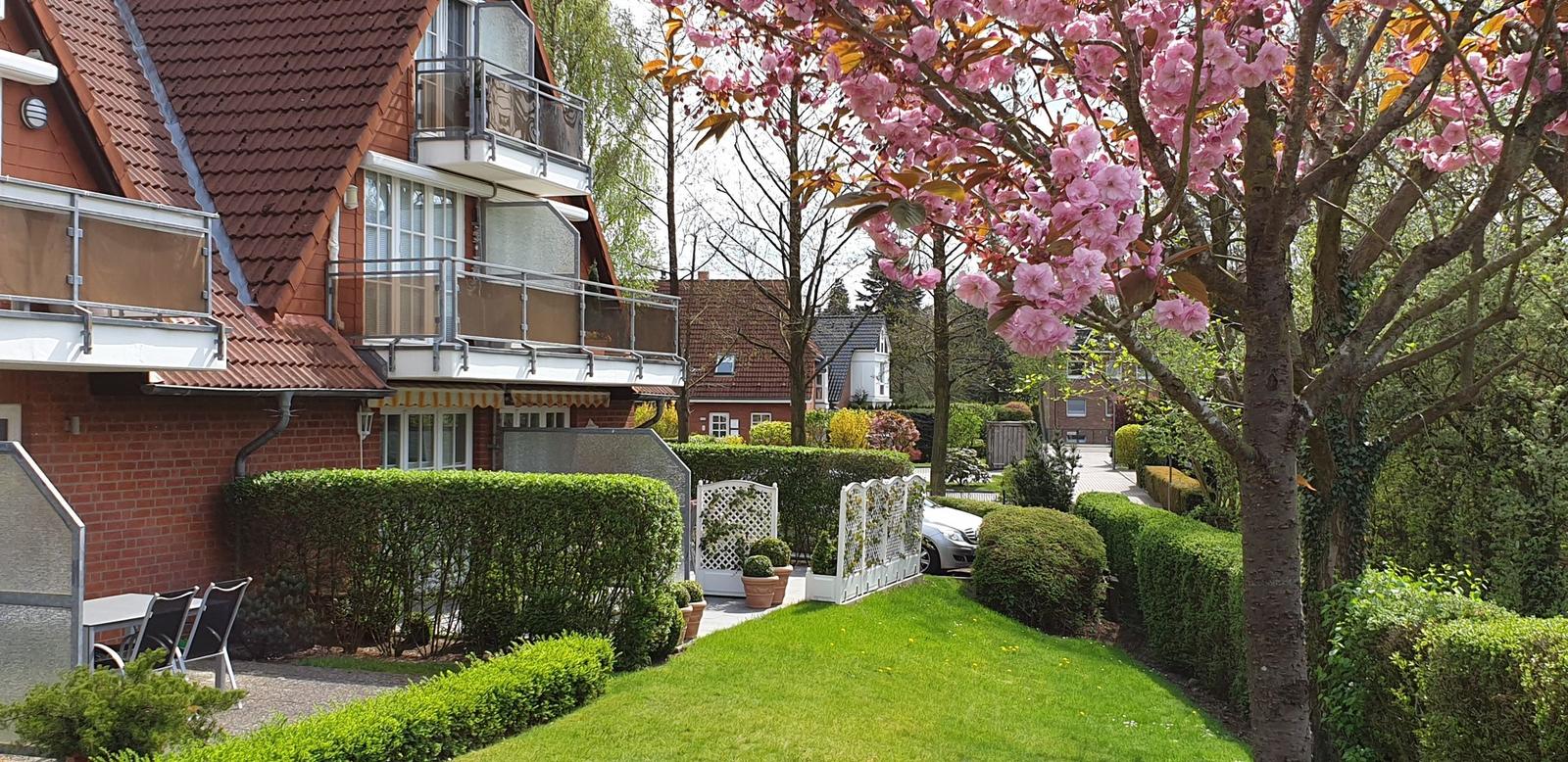 Haus mit Balkon, Garten und blühendem Baum im Vordergrund.