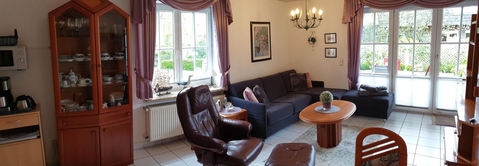 Wohnzimmer mit Sofa, Ledersessel und Glasvitrine. Blick auf Garten durch Fenster.