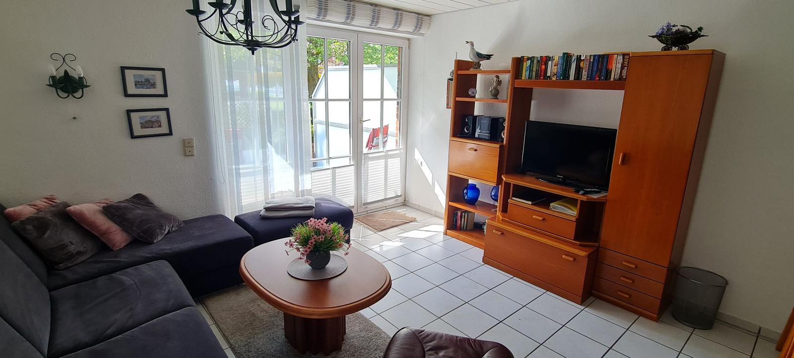 Wohnzimmer mit Sofa, Couchtisch und TV-Möbel. Durchgang zum Garten.