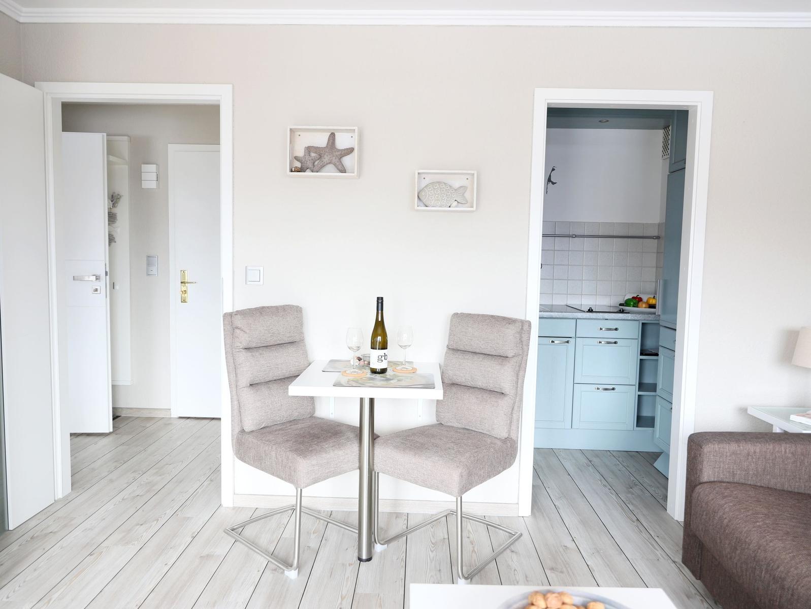 Essbereich mit Tisch und zwei Stühlen. Küche und Flur sind sichtbar.