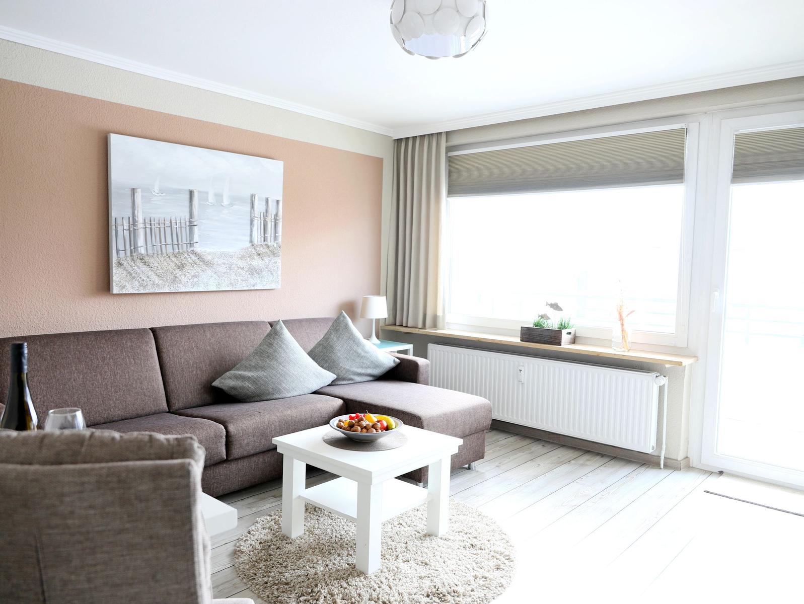 Wohnzimmer mit Sofa, Tisch und Fenster. Wandbild und Teppich sind sichtbar.