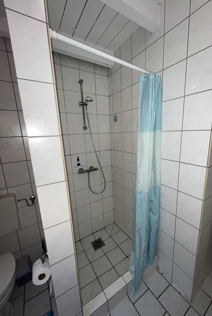 Shower with showerhead, shower curtain, and toilet in a bathroom.