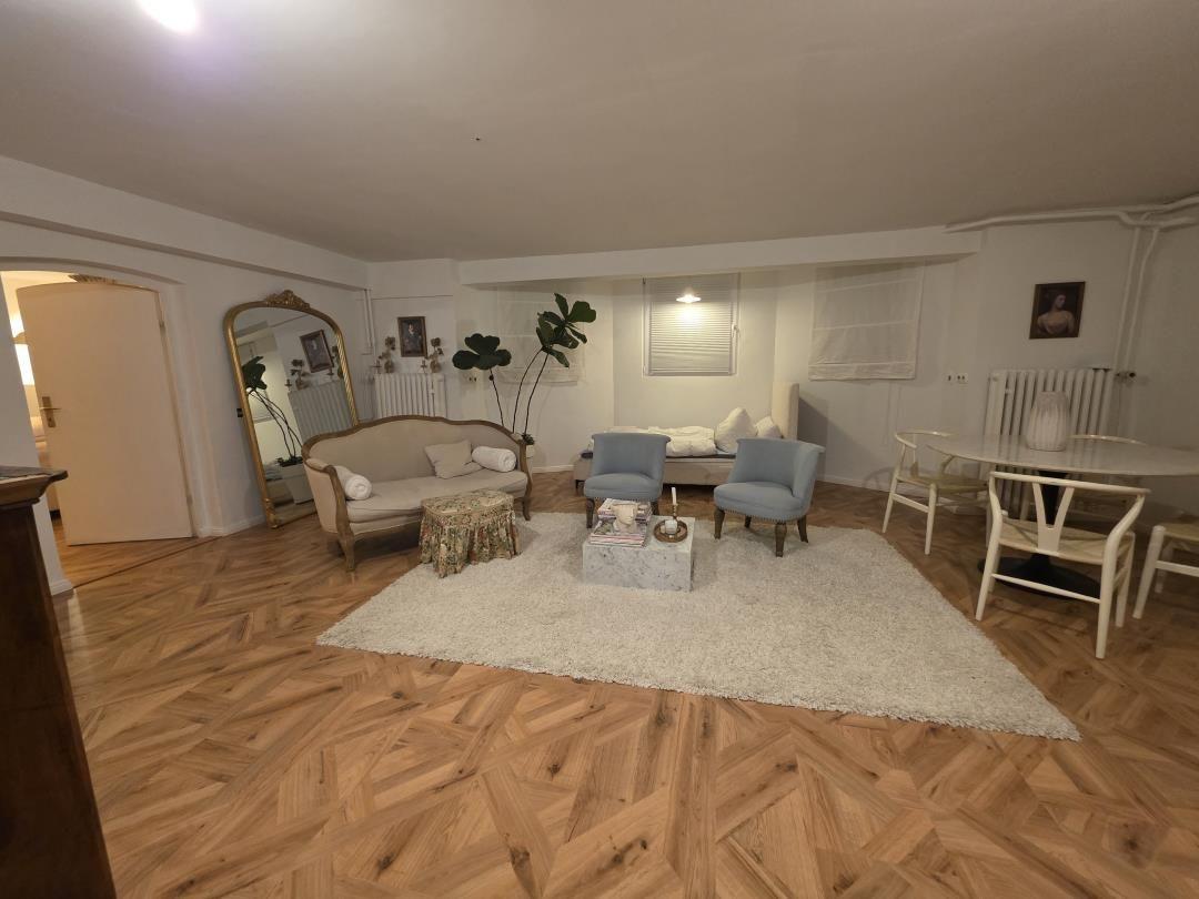 Living room with wooden floor, sofa, armchairs, and dining table