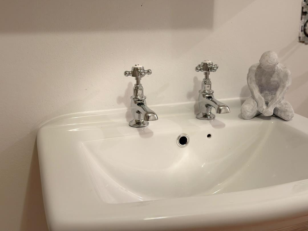 White sink with two faucets and a sculpture beside it.