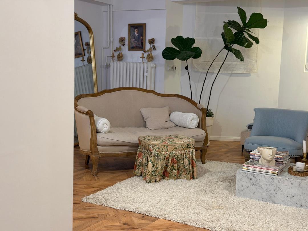 A living room with sofa, armchair, and plant on wooden floor.