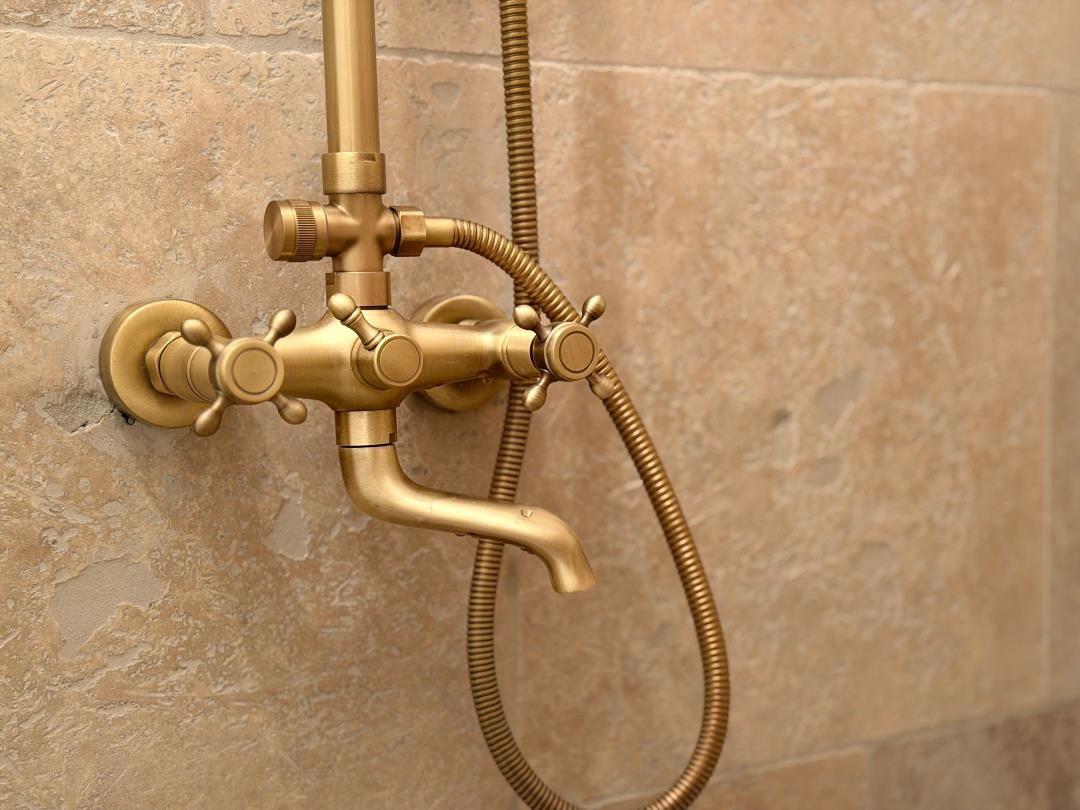 Gold shower with handheld showerhead and faucet on stone wall
