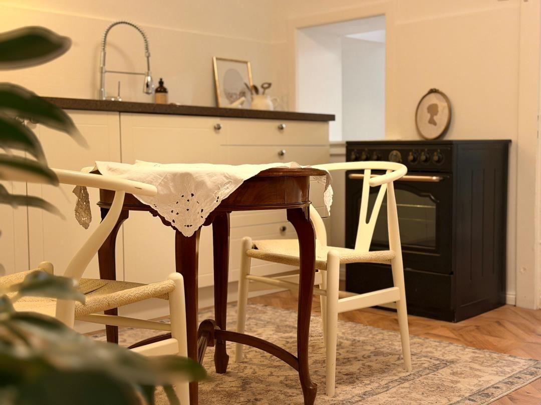 Dining table with chairs in front of kitchen with stove and sink.