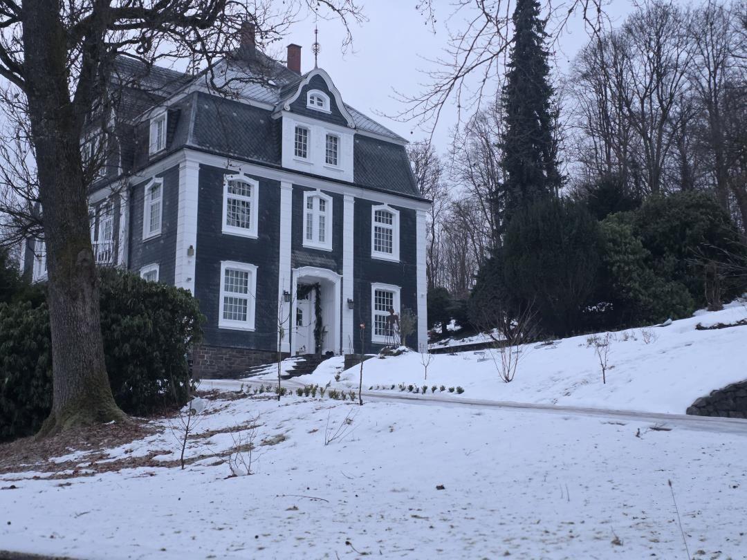 Manor-style house with white plaster and dark slate roof in the snow.