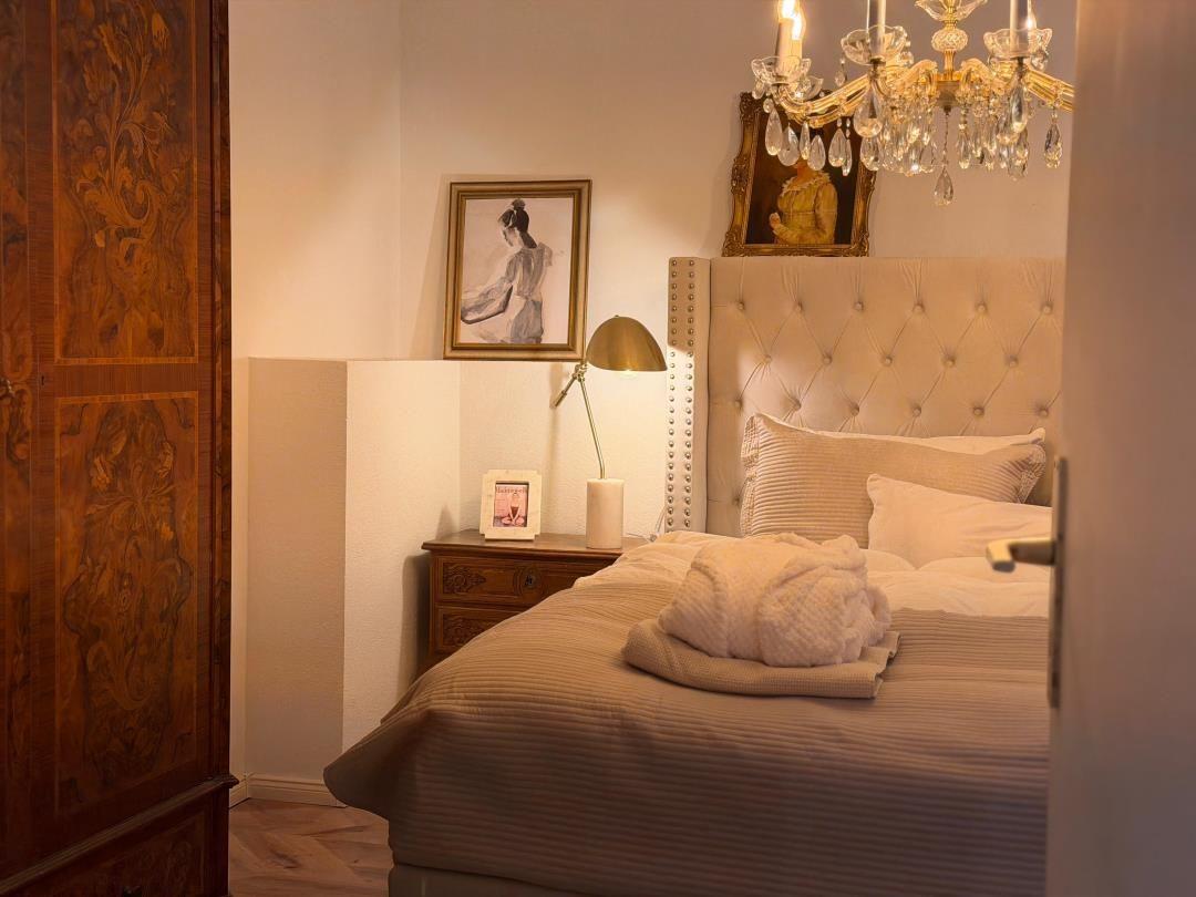 Bedroom with bed, nightstand, chandelier, and wooden wardrobes.