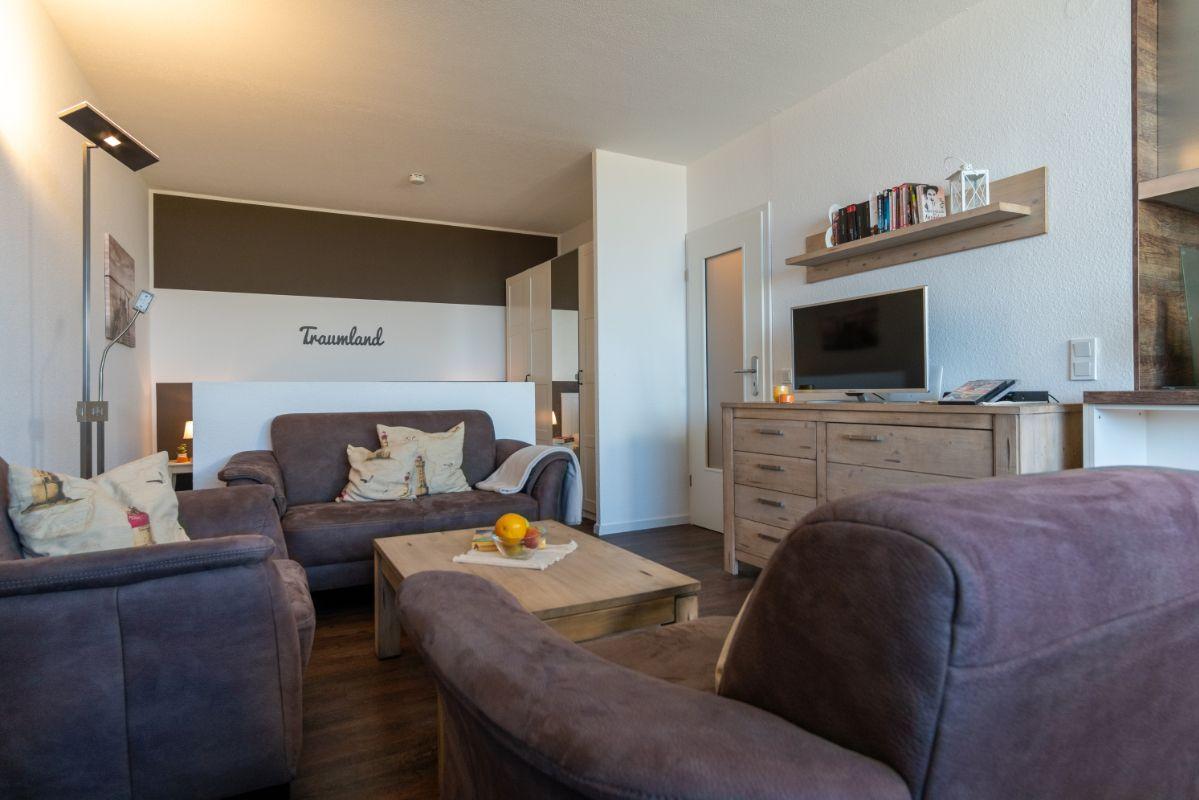 Wohnzimmer mit Sofa, Couchtisch und Fernseher. Wand mit Schriftzug Traumland.