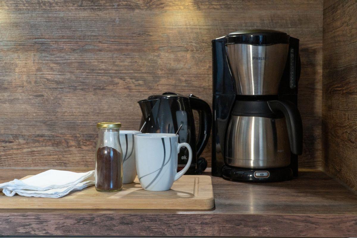 Kaffeemaschine, Kanne, Tassen und Kaffeebohnen auf Holzoberfläche.