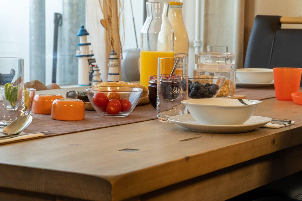 Frühstückstisch mit Obst, Getränken und Geschirr vor Fenster mit Leuchtturmdekoration