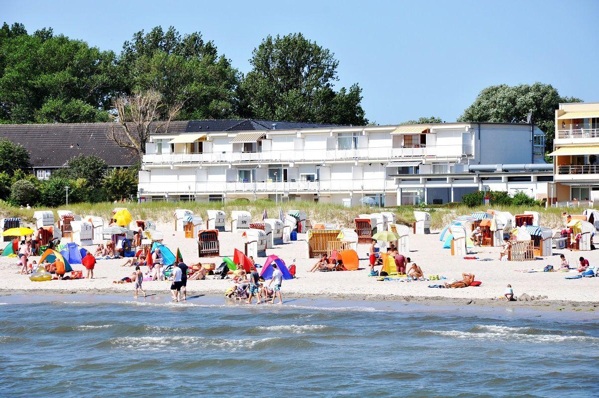 Strand mit bunten Strandkörben und Gästen vor einer Ferienwohnung.