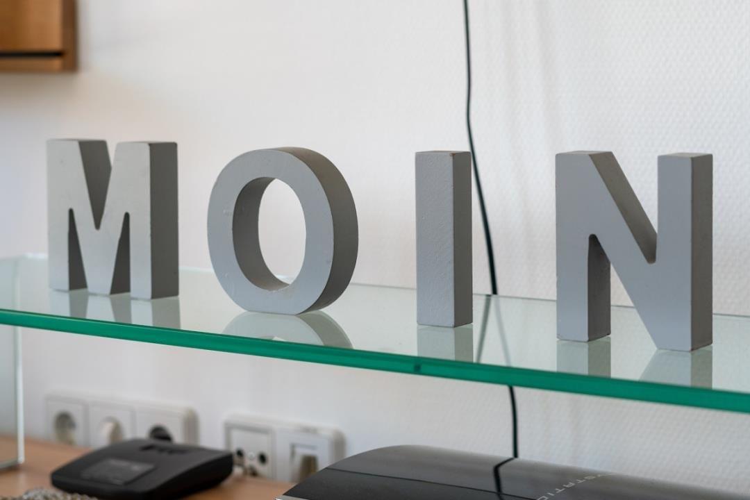 Glasregal mit grauen Buchstaben MOIN und Steckdosen darunter