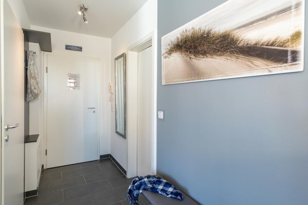 Flur mit Wandbild, Spiegel und Garderobe. Bodenfliesen und blaue Wand.