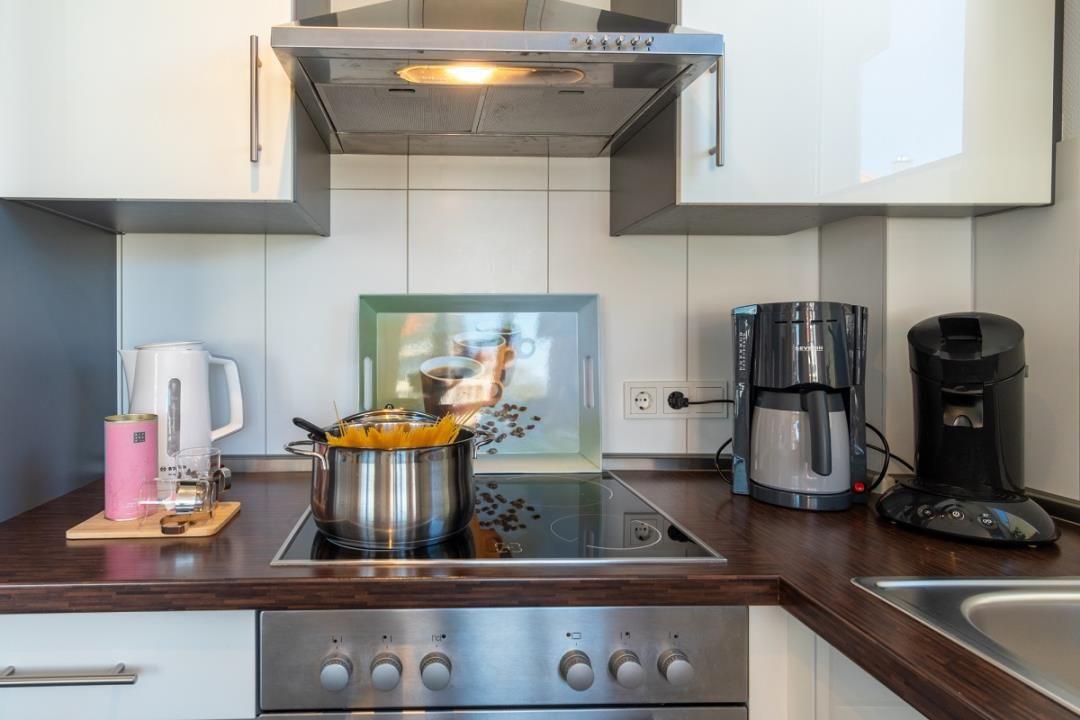 Küche mit Herd, Dunstabzug, Kaffeemaschine und Kochtopf.