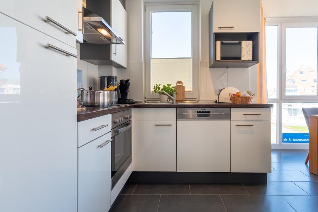 Moderne Küche mit weißen Schränken, Edelstahlgeräten und dunklem Arbeitsplatz.