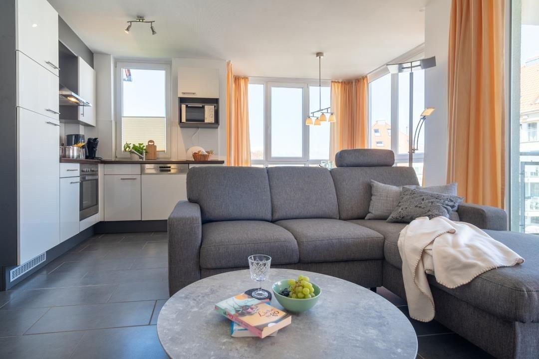 Wohnbereich mit Sofa, Küchenzeile und großen Fenstern.