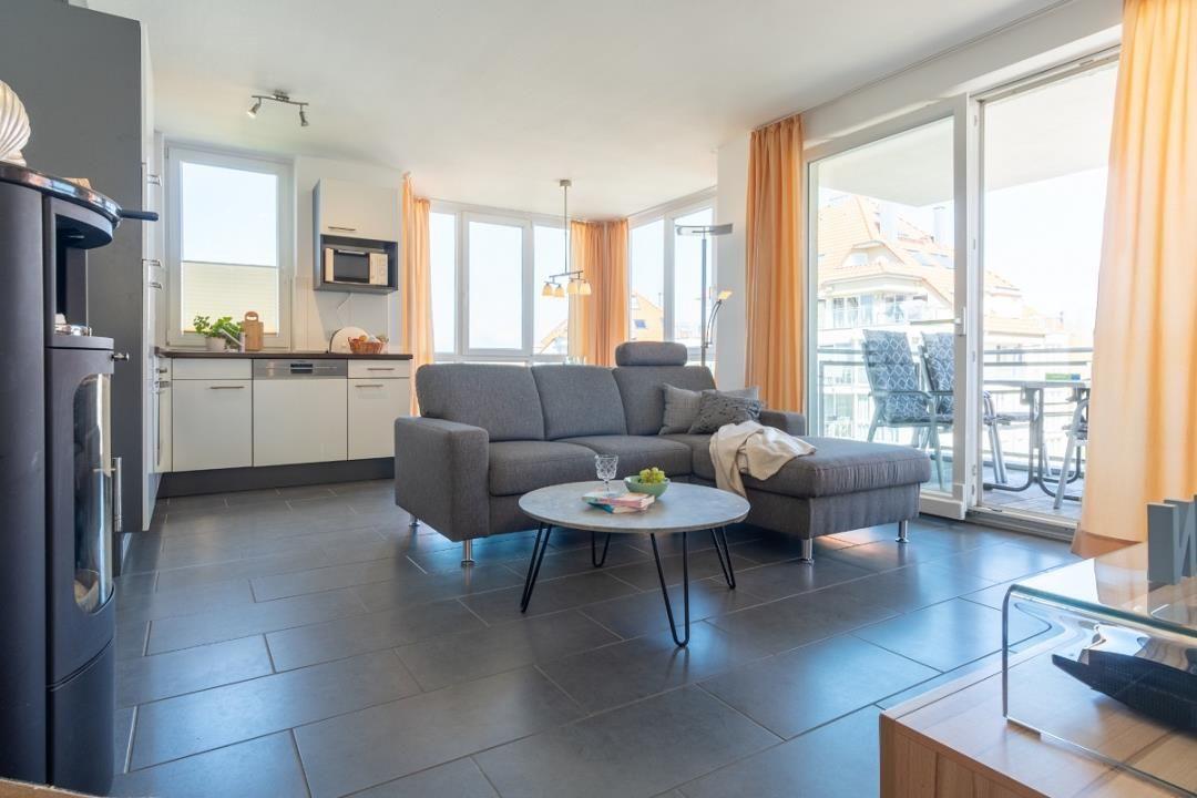 Wohnung mit Küche, Sofa und Balkon mit Stühlen.