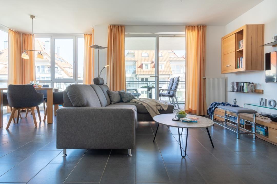 Wohnbereich mit Sofa, Tisch und Balkonansicht.