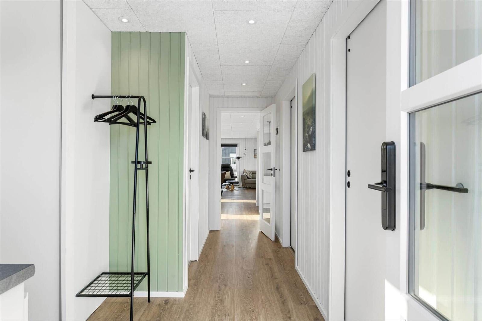 Hallway with coat rack, wooden floor, and view into living area.