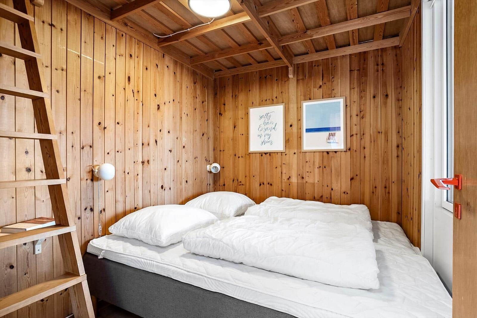 Bedroom with wooden walls, bed, ladder, and window.