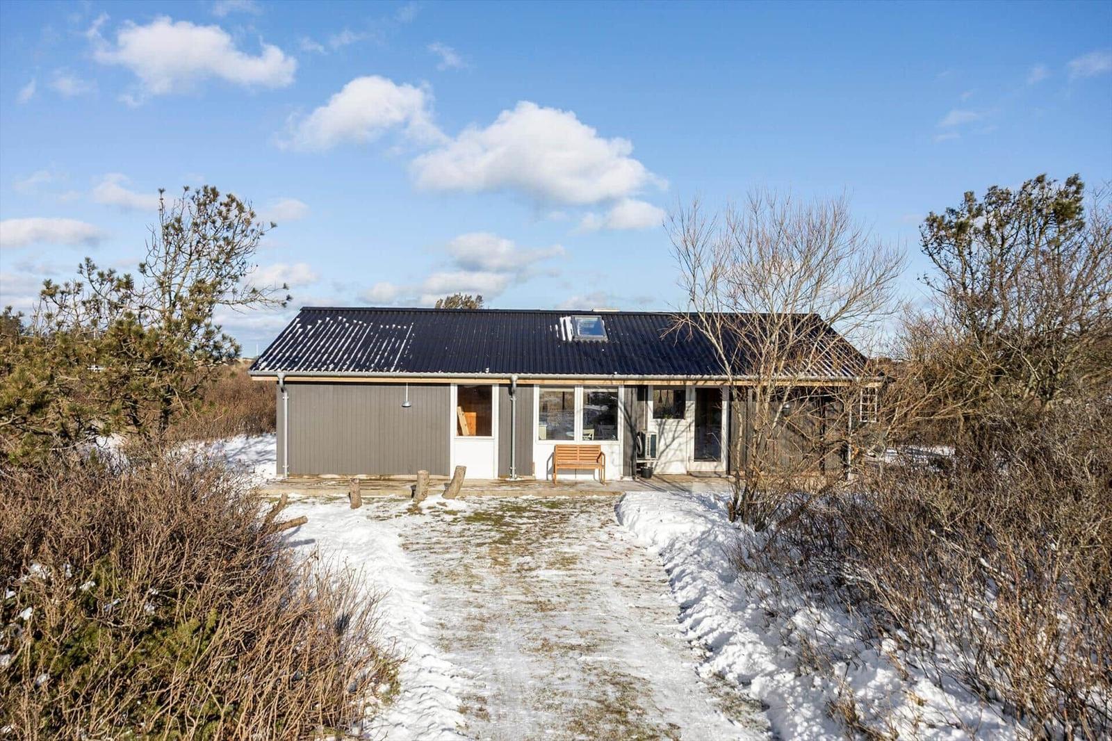 Single-family house with snow-covered roof and wooden bench in front of entrance.