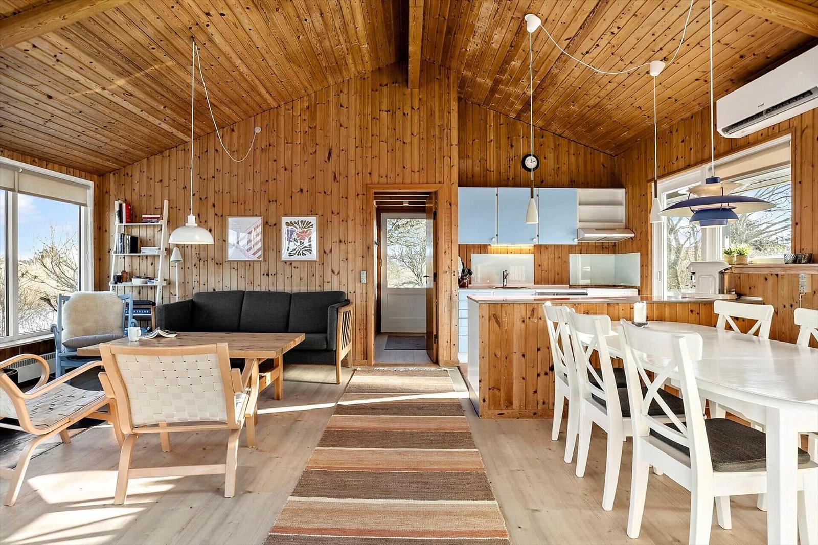 Living and dining area with wooden walls, kitchen island, and dining table.