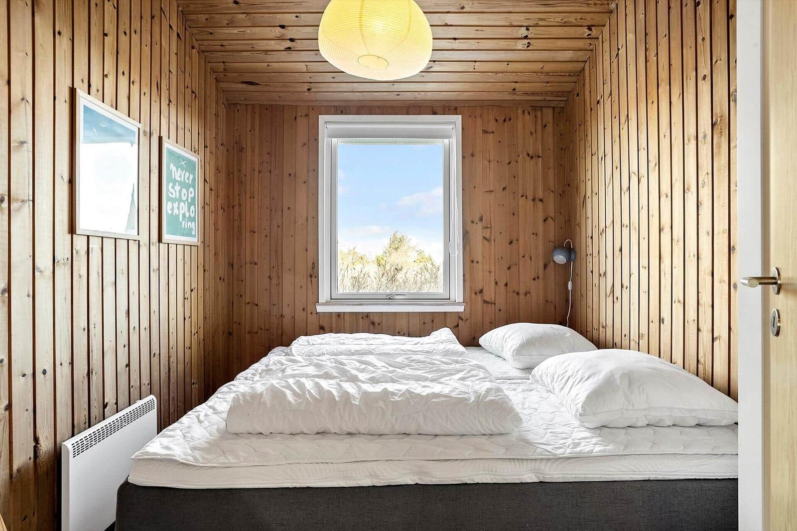 Bedroom with wooden walls, bed, and window with view of trees.