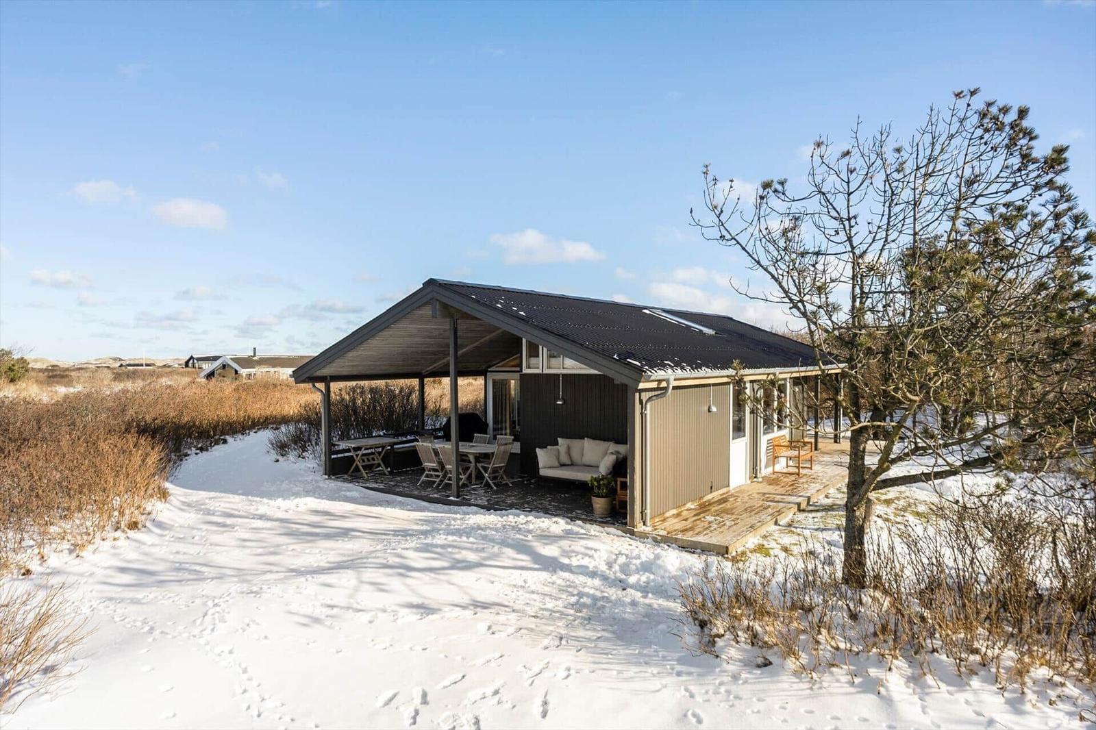 Modern cabin with covered outdoor area, seating, and snow cover.