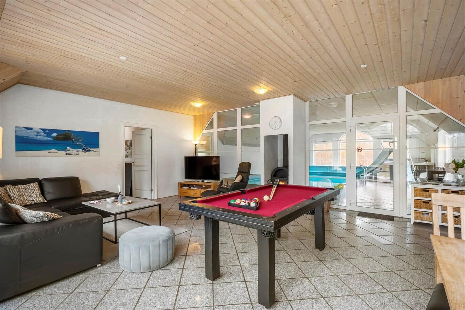 Ein Raum mit Billardtisch, Sofa und Blick auf die Poolanlage.
