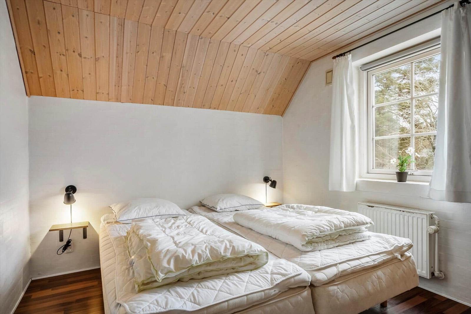 Zimmer mit zwei Betten, Holzdecke und Fenster mit Blick auf Bäume.