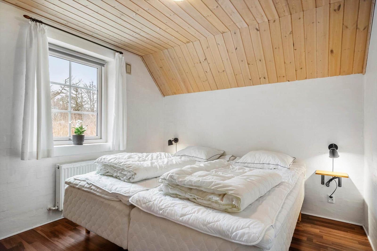 Schlafzimmer mit Doppelbett, Holzdecke und Fenster mit Blick.