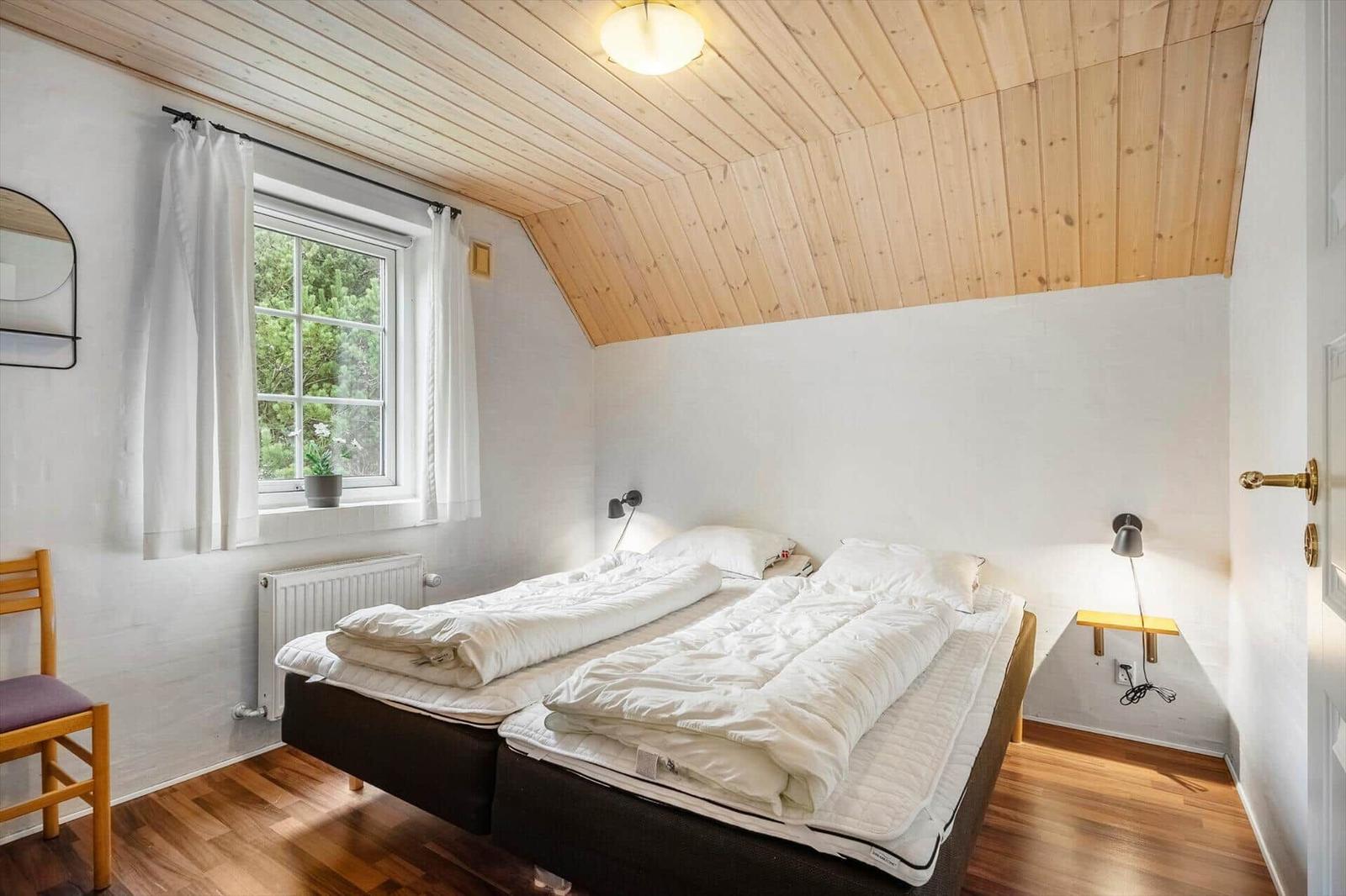 Schlafzimmer mit Doppelbett, Holzdecke und Fenster mit Blick auf Grün.