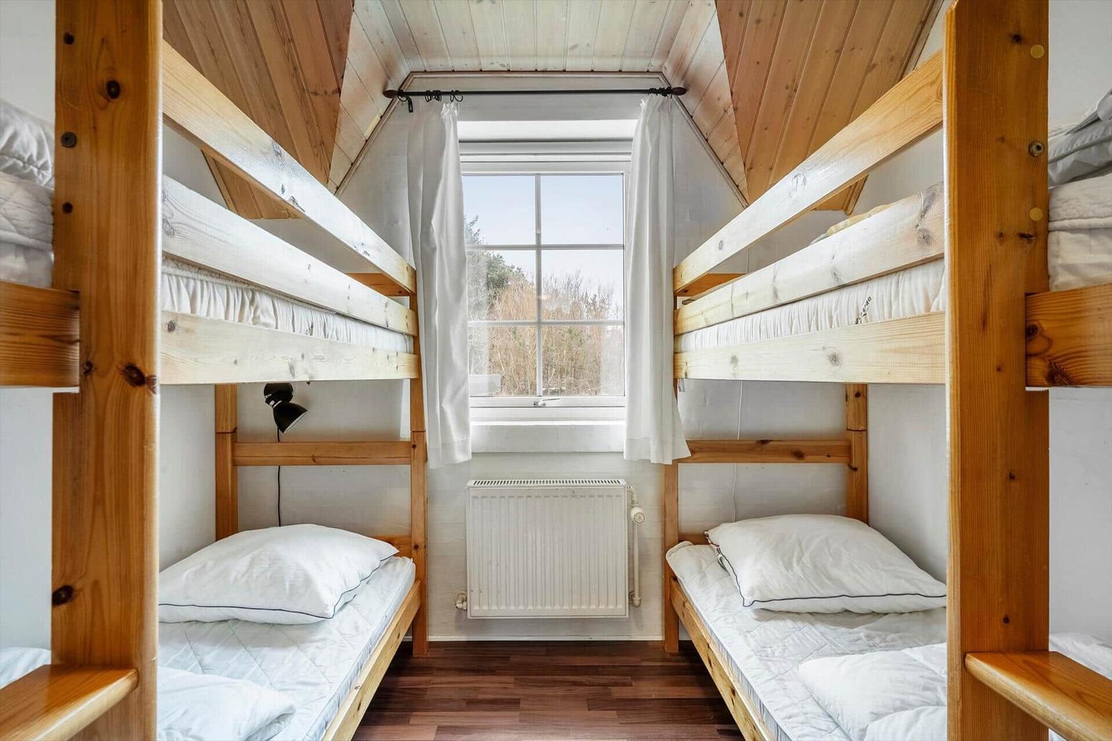 Zwei Etagenbetten mit weißen Matratzen und Kissen. Holzdecke, Fenster mit Vorhängen.