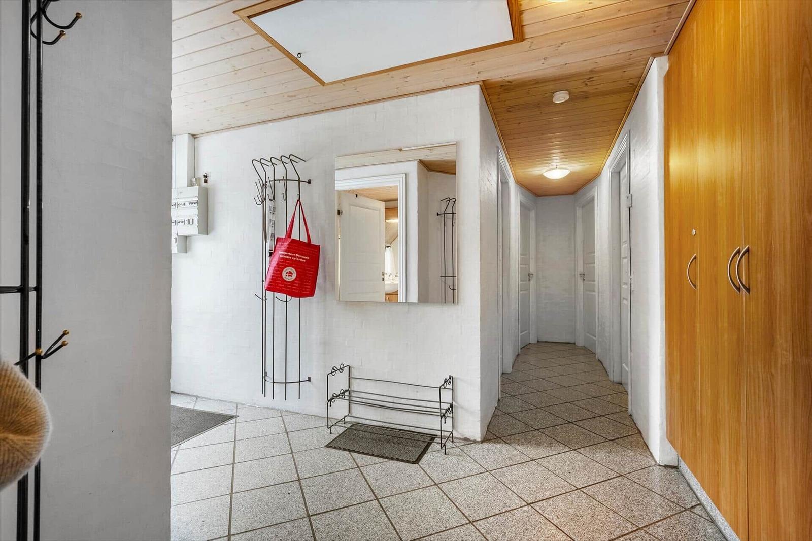 Flur mit Holzdecke, weißen Wänden und Bodenfliesen. Ankleidekörbe und Spiegel sind sichtbar.
