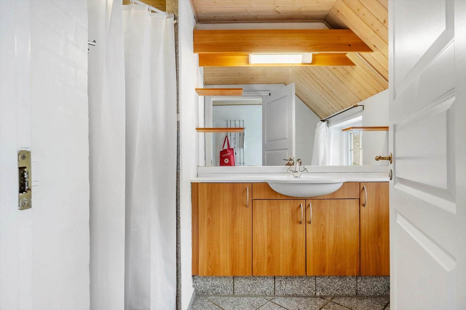 Badezimmer mit Holzregalen, Waschbecken und Dusche unter Dachschrägen.