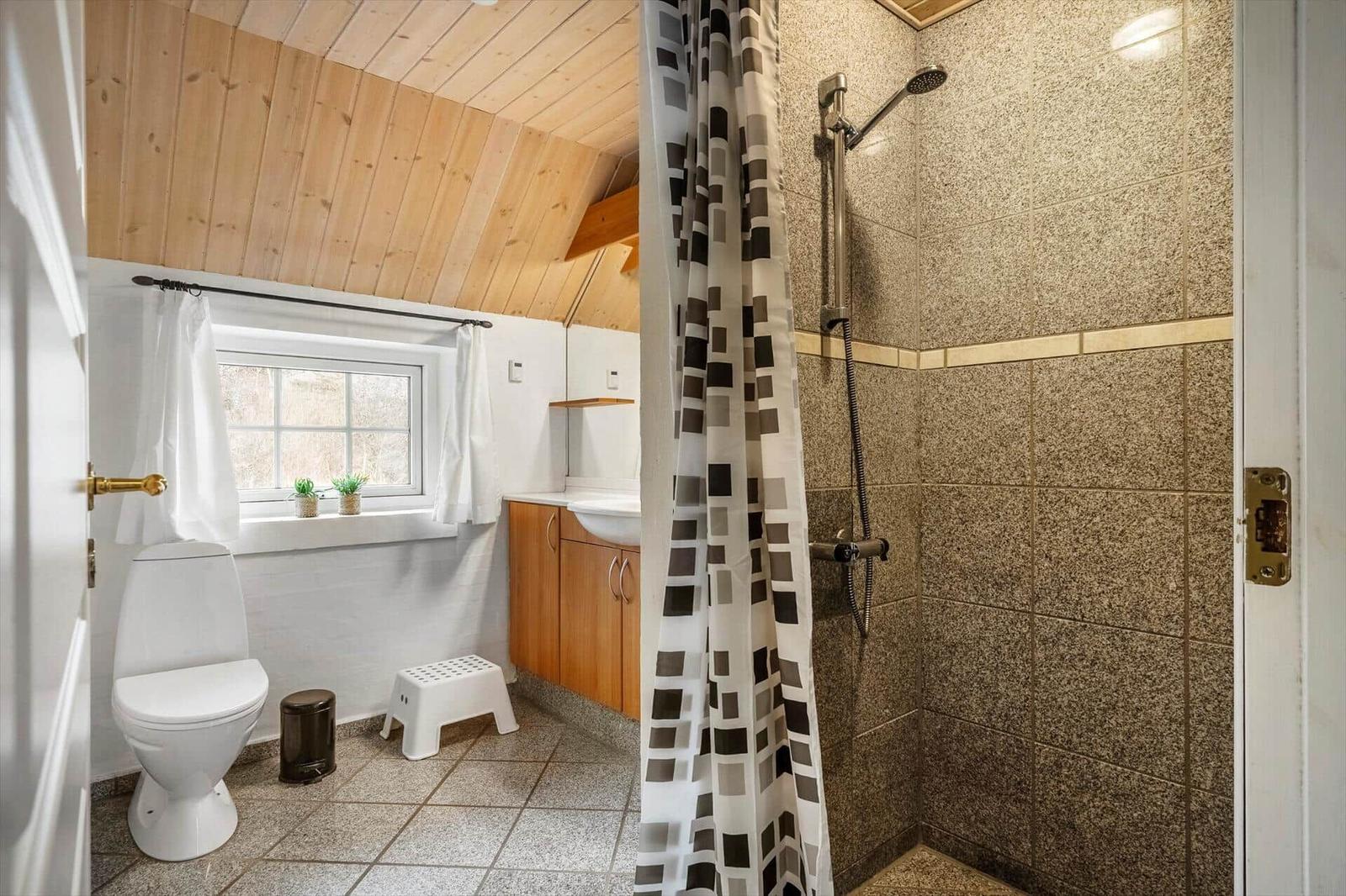 Badezimmer mit Dusche, Toilette und Waschbecken unter Holzdecke.